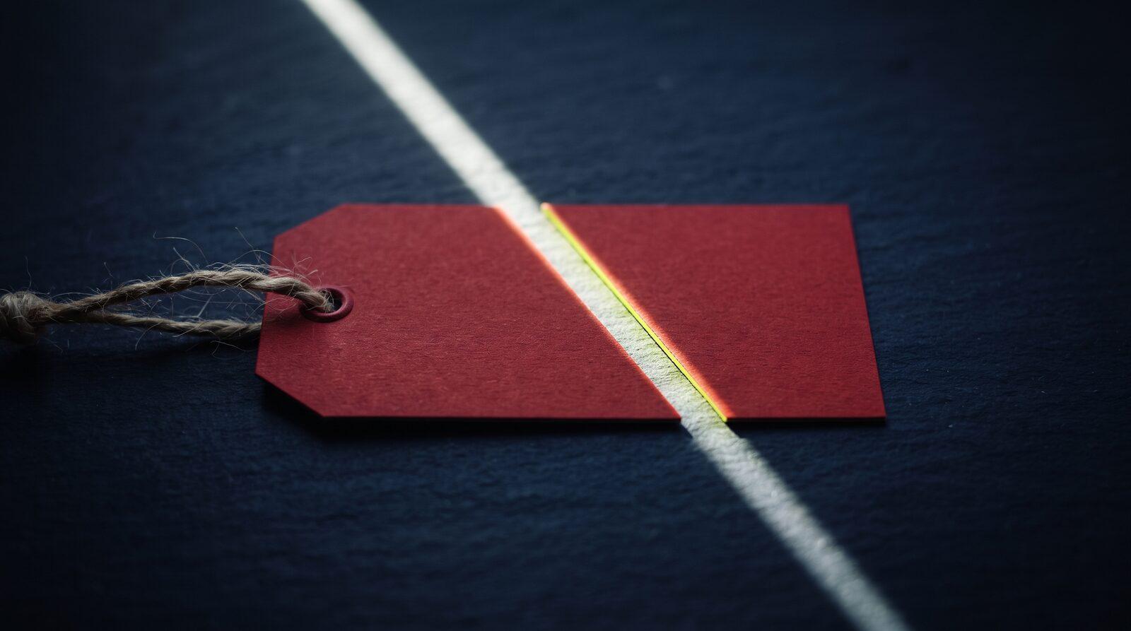 A red discount price tag cut in half by a blade of light on dark navy stone